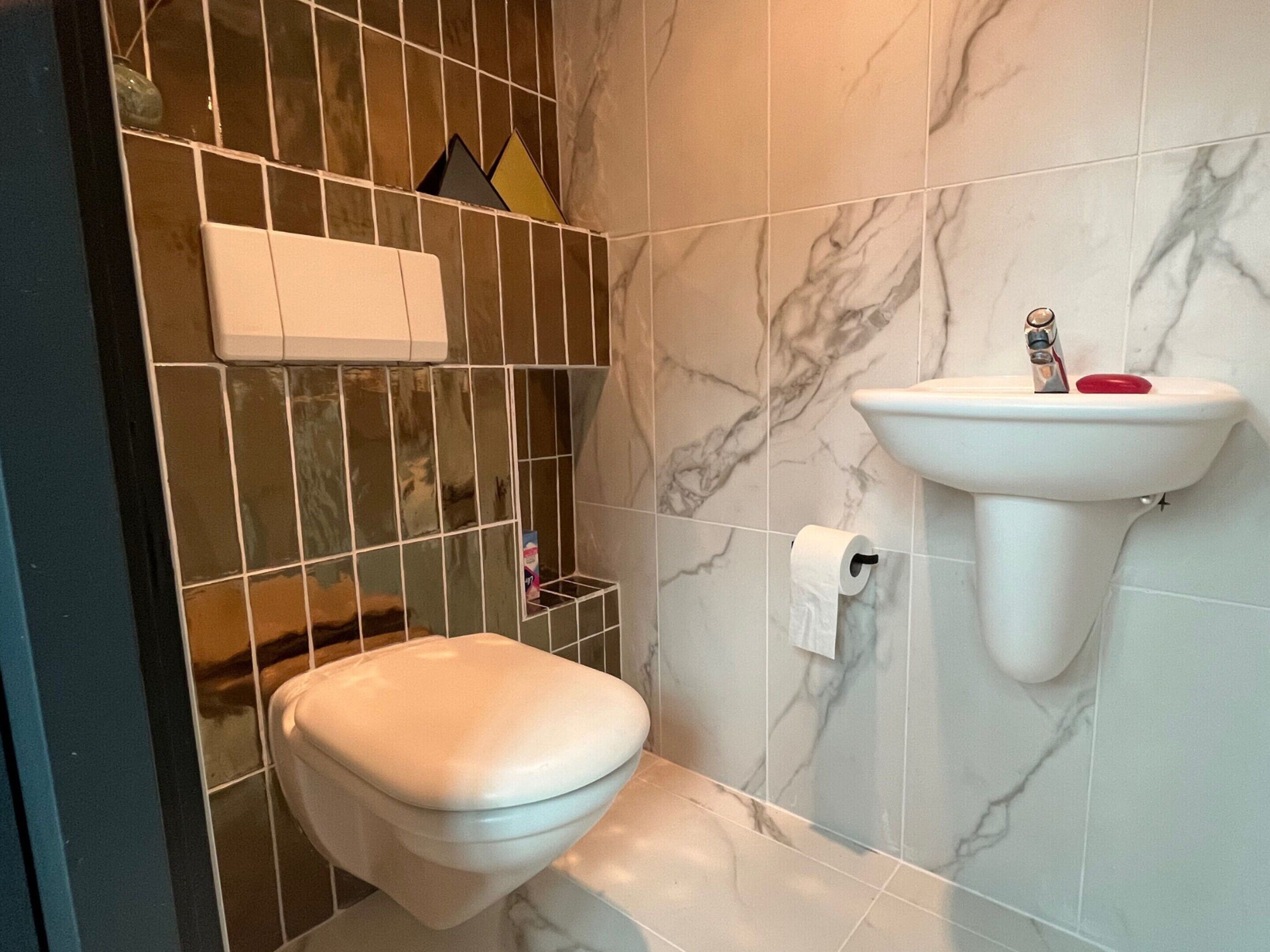 Un baño con inodoro, lavamanos y pared de azulejos de mármol.