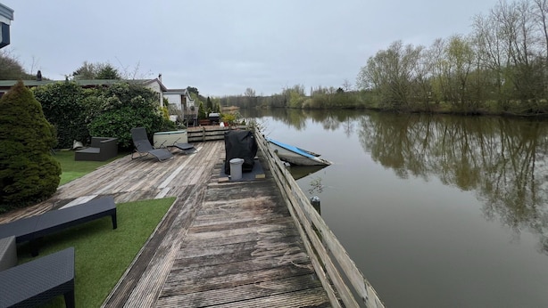 Une terrasse en bois avec des sièges extérieurs et une vue sur une rivière paisible.