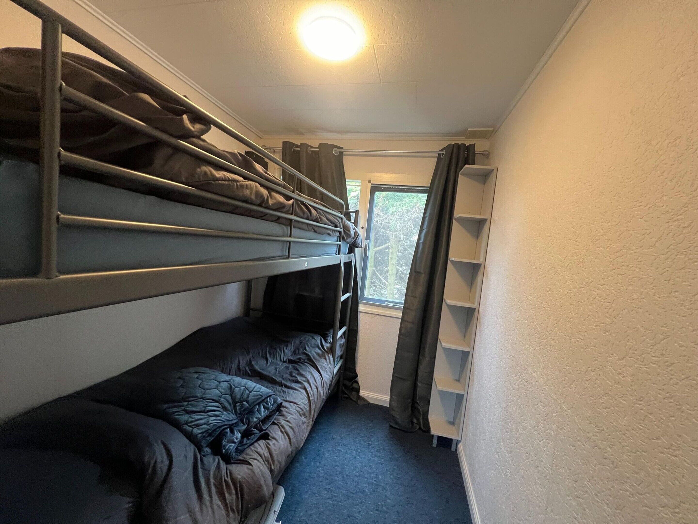 A bunk bed room with a window and a shelf unit.