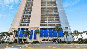 Un grand hôtel à la façade beige et aux auvents bleus, composé de plusieurs étages et doté d’une entrée principale.