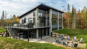 A modern two-story house with a covered deck, outdoor seating area, and a fire pit. - Incredible View with Spa | L'Ivresse des Sommets (Saint-Côme)
