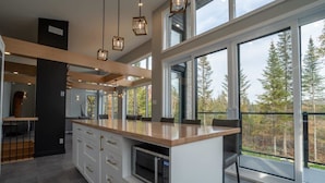 A modern kitchen with large windows, a wooden countertop, and a built-in microwave. - Incredible View with Spa | L'Ivresse des Sommets (Saint-Côme)