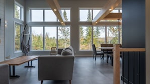 A spacious living area with a sofa, dining table, and chairs, large windows offering a view of trees and a building. - Incredible View with Spa | L'Ivresse des Sommets (Saint-Côme)