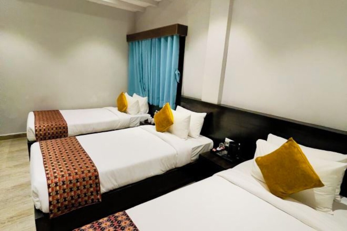 Habitación de hotel con tres camas, un ventanal grande con cortinas azules y un cabecero de madera oscura.