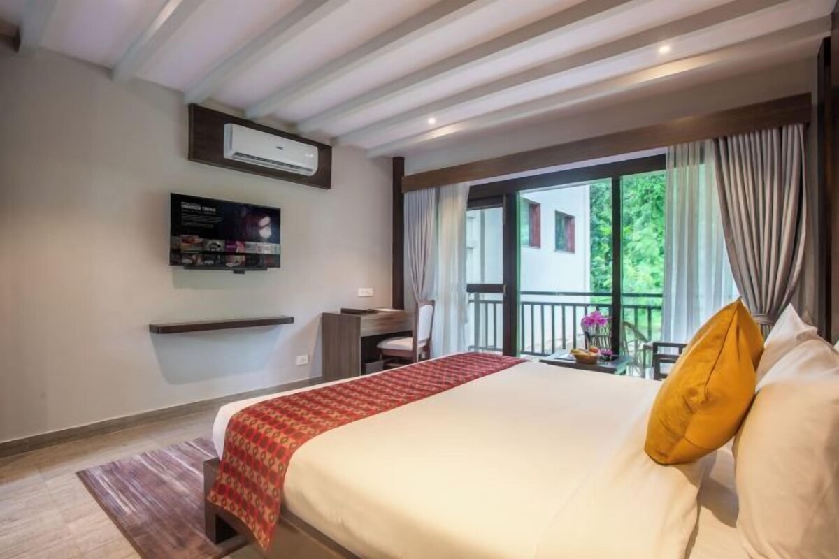 A hotel room with a bed, a TV mounted on the wall, a desk, and a balcony with curtains.