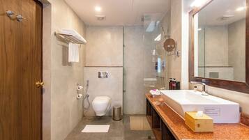 Un bagno moderno con porta in legno, un water bianco, una doccia vetrata e un piano lavabo in marmo con lavandino e articoli da toilette.