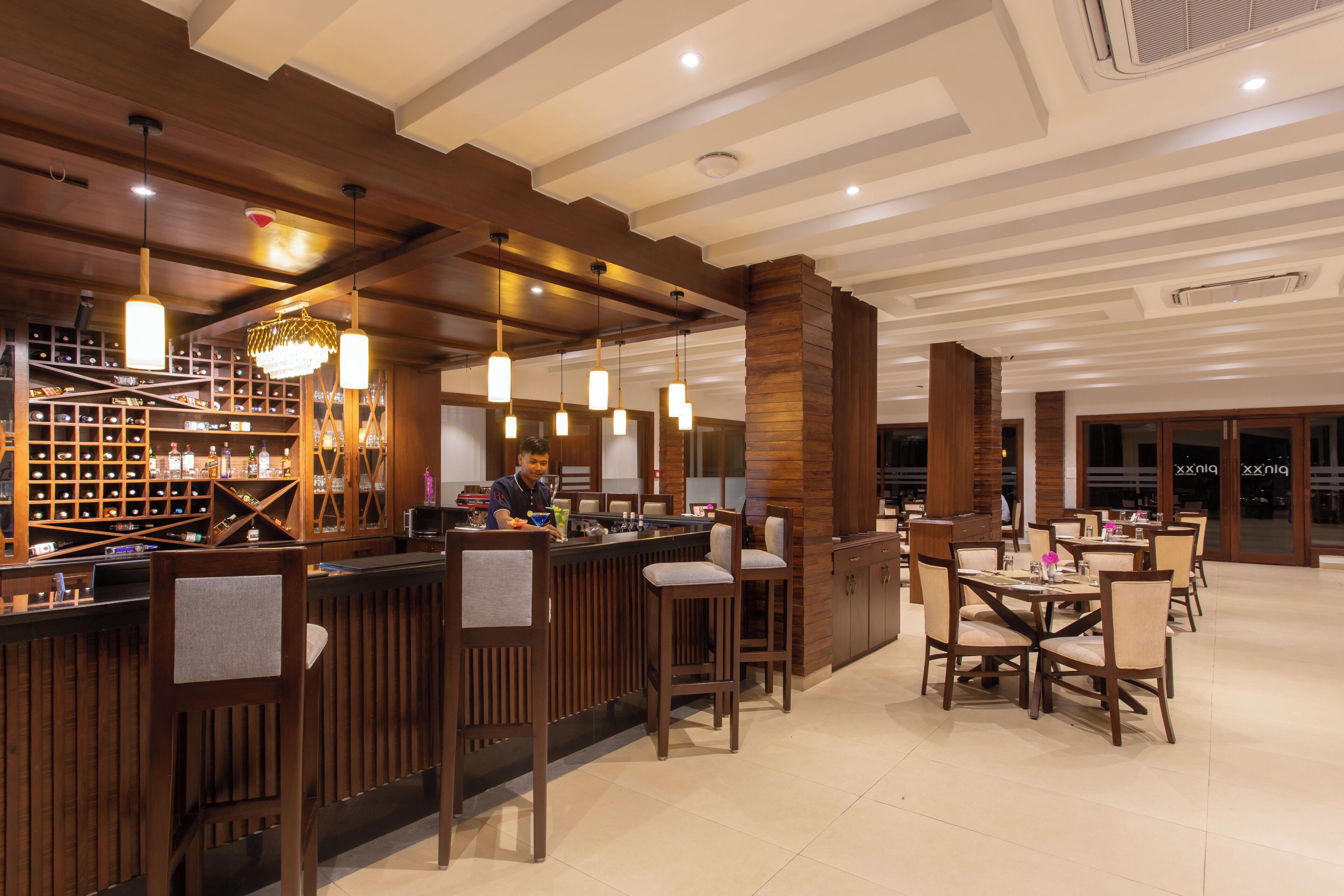 Una zona de bar moderna con mostradores de madera, lámparas colgantes y una estantería para vinos.