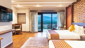 Habitación de hotel con cama, escritorio, silla y balcón con vista a la montaña.