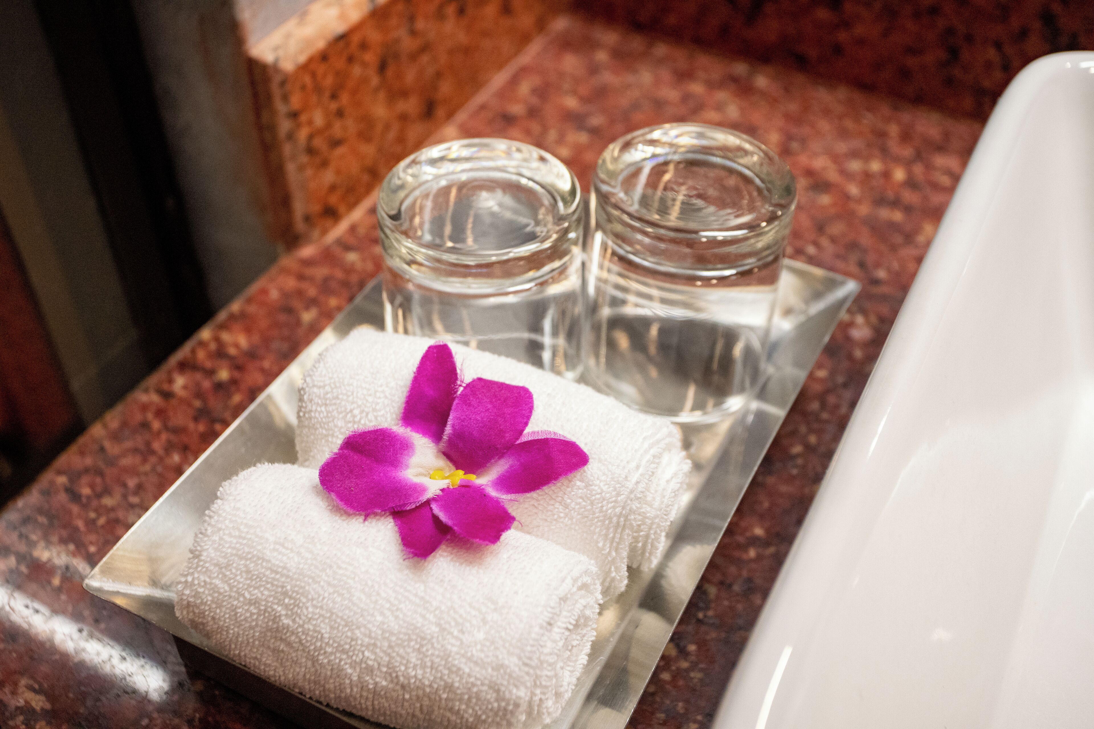 A bathroom with a white towel and a purple orchid on a tray, two glass bottles, and a white bathtub.