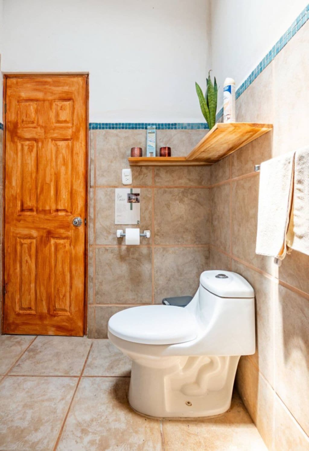 Een badkamer met een houten deur, een toilet, een plank met toiletartikelen en een handdoek aan de muur.