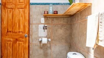 Een badkamer met een houten deur, een toilet, een plank met toiletartikelen en een handdoek aan de muur.