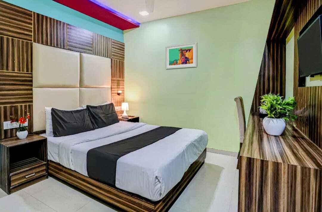 A modern hotel room with a large bed, wooden paneling on the walls, a flat-screen TV, and a small table with a plant.