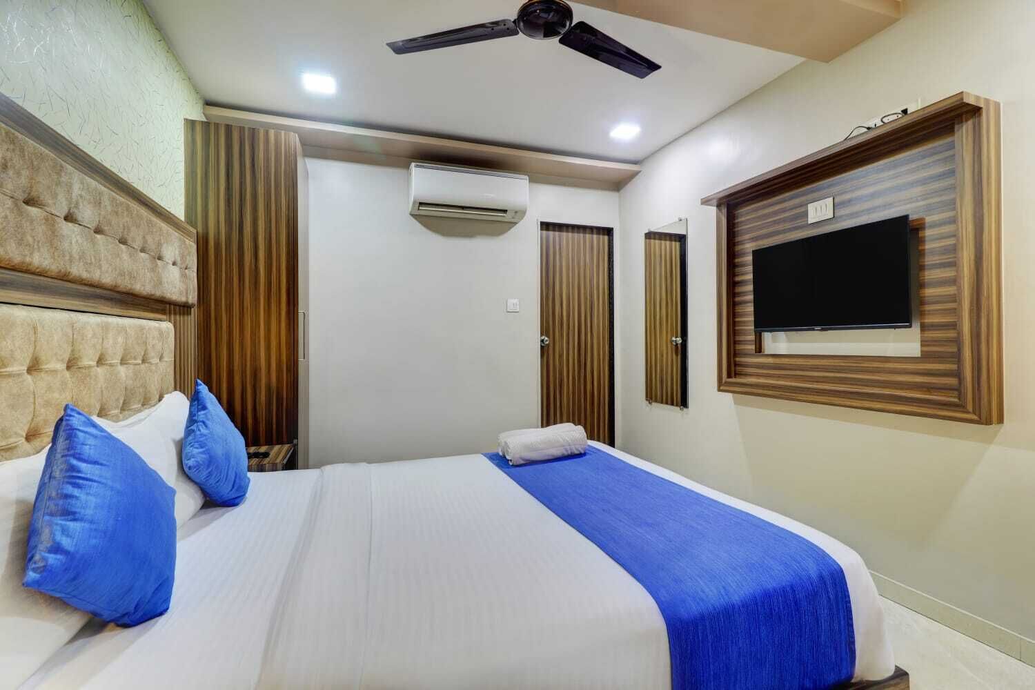 A hotel room with a large bed, a ceiling fan, an air conditioning unit, and a television on the wall.