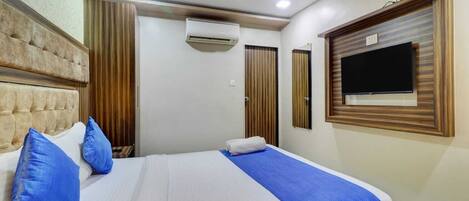 A hotel room with a large bed, a ceiling fan, an air conditioning unit, and a television on the wall.