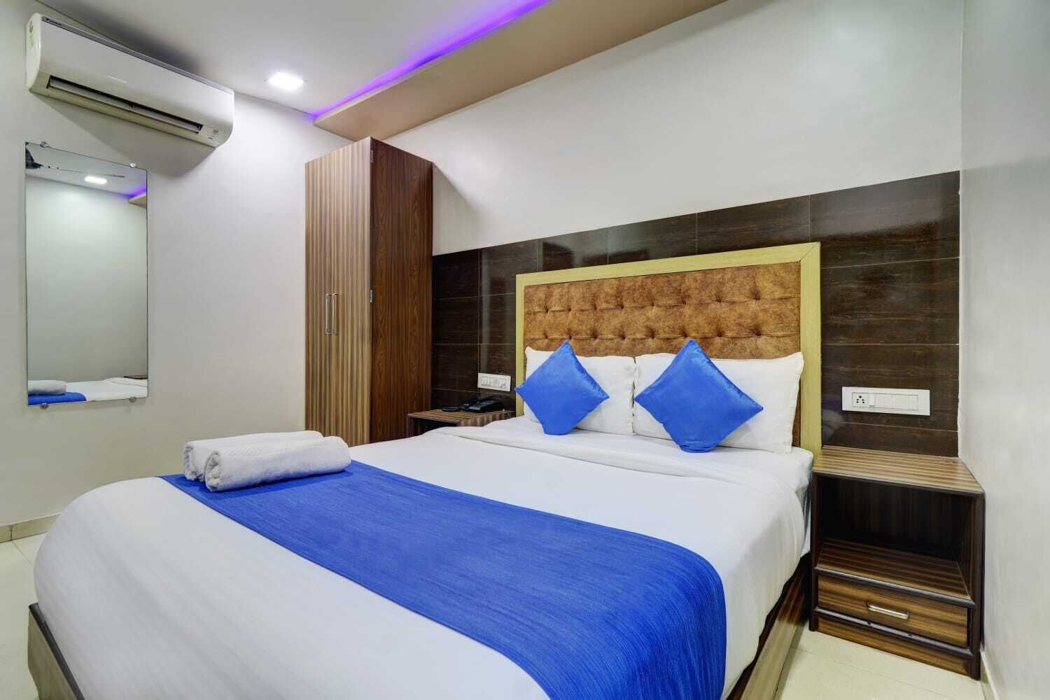 Una habitación de hotel con cama, mesita de noche, equipo de aire acondicionado, espejo y armario de madera.