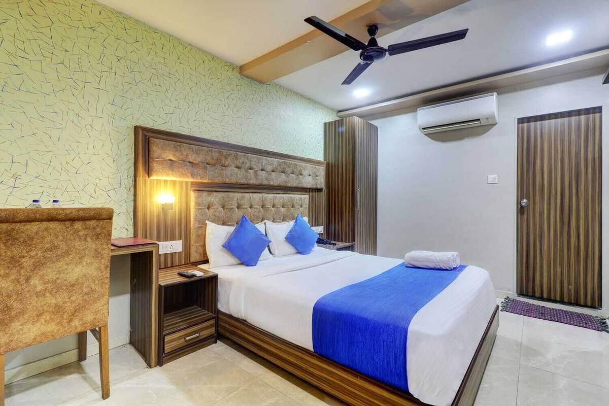 Une chambre d’hôtel comprenant un lit, un bureau, une chaise, un ventilateur de plafond, un appareil de climatisation et une armoire.