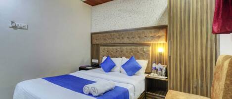 Hotelkamer met een bed, nachtkastje, stoel, plafondventilator en een wandlamp.
