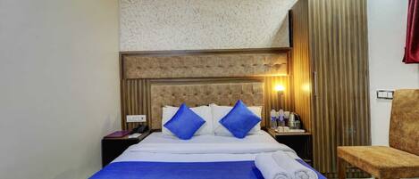 A hotel room with a bed, a chair, a nightstand, and a wall-mounted lamp.