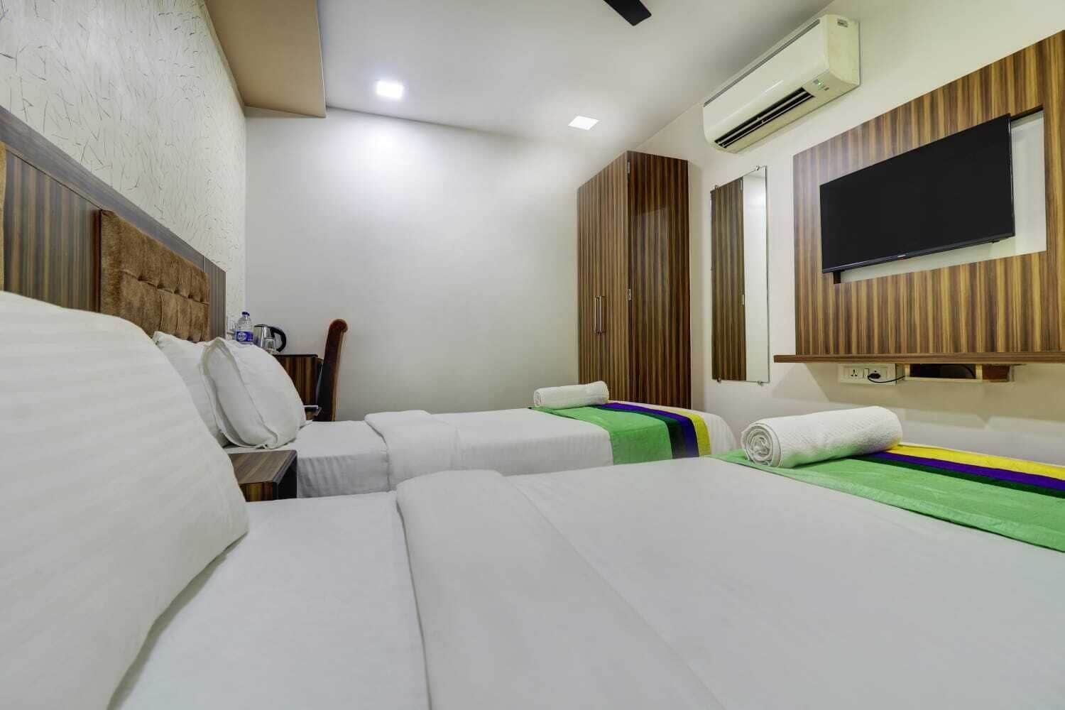 A hotel room with two beds, a wooden headboard, a flat-screen TV, and an air conditioning unit.