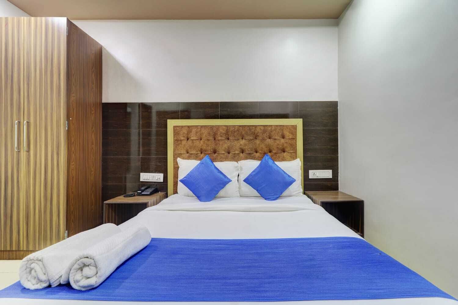 A hotel room with a large bed, two nightstands, a wooden wardrobe, and a blue bedspread.