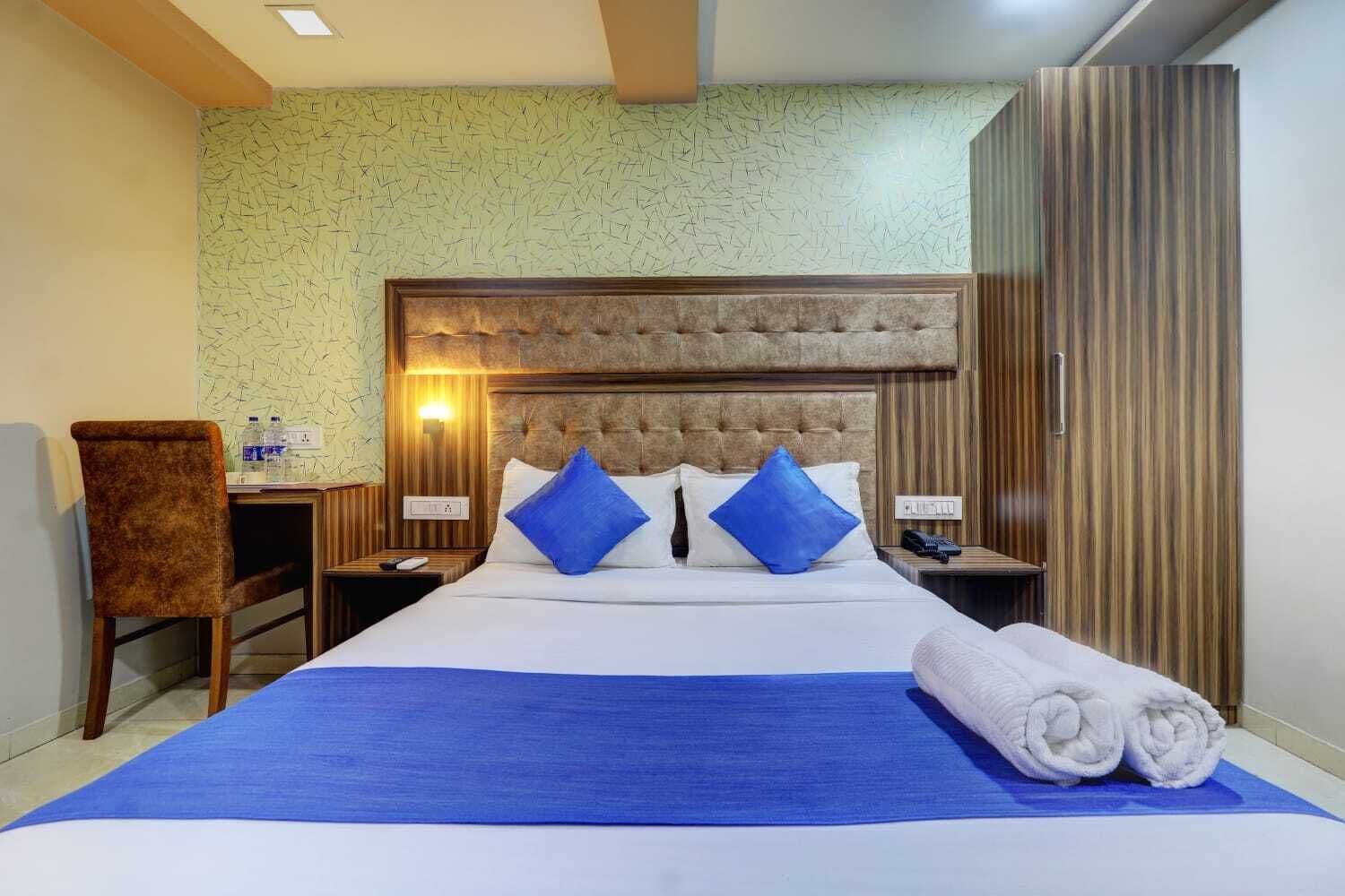 A hotel room with a large bed, two nightstands, a chair, and a wardrobe.