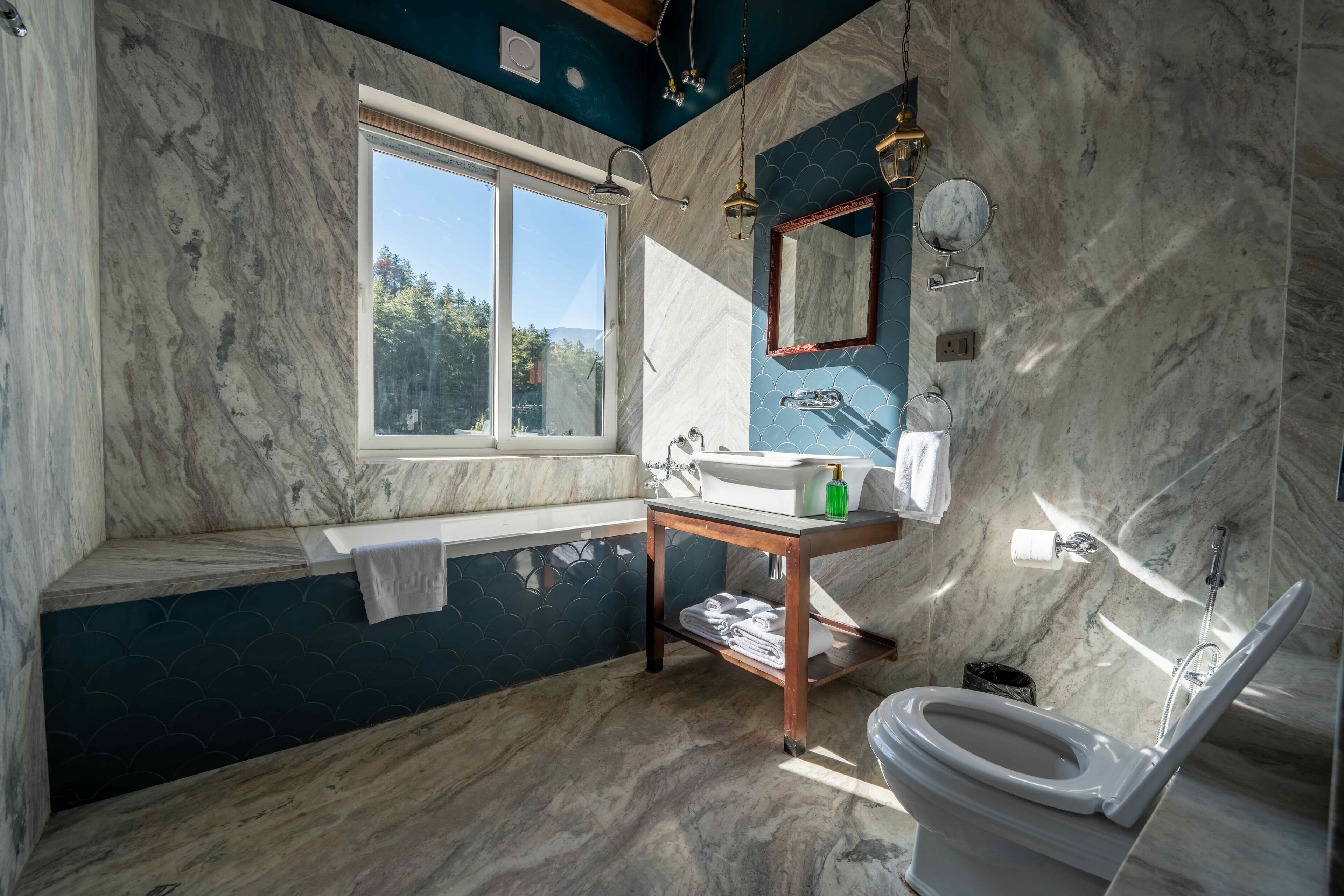 Ein Badezimmer mit Marmorwand, Fenster, Waschbecken, Toilette und Dusche.