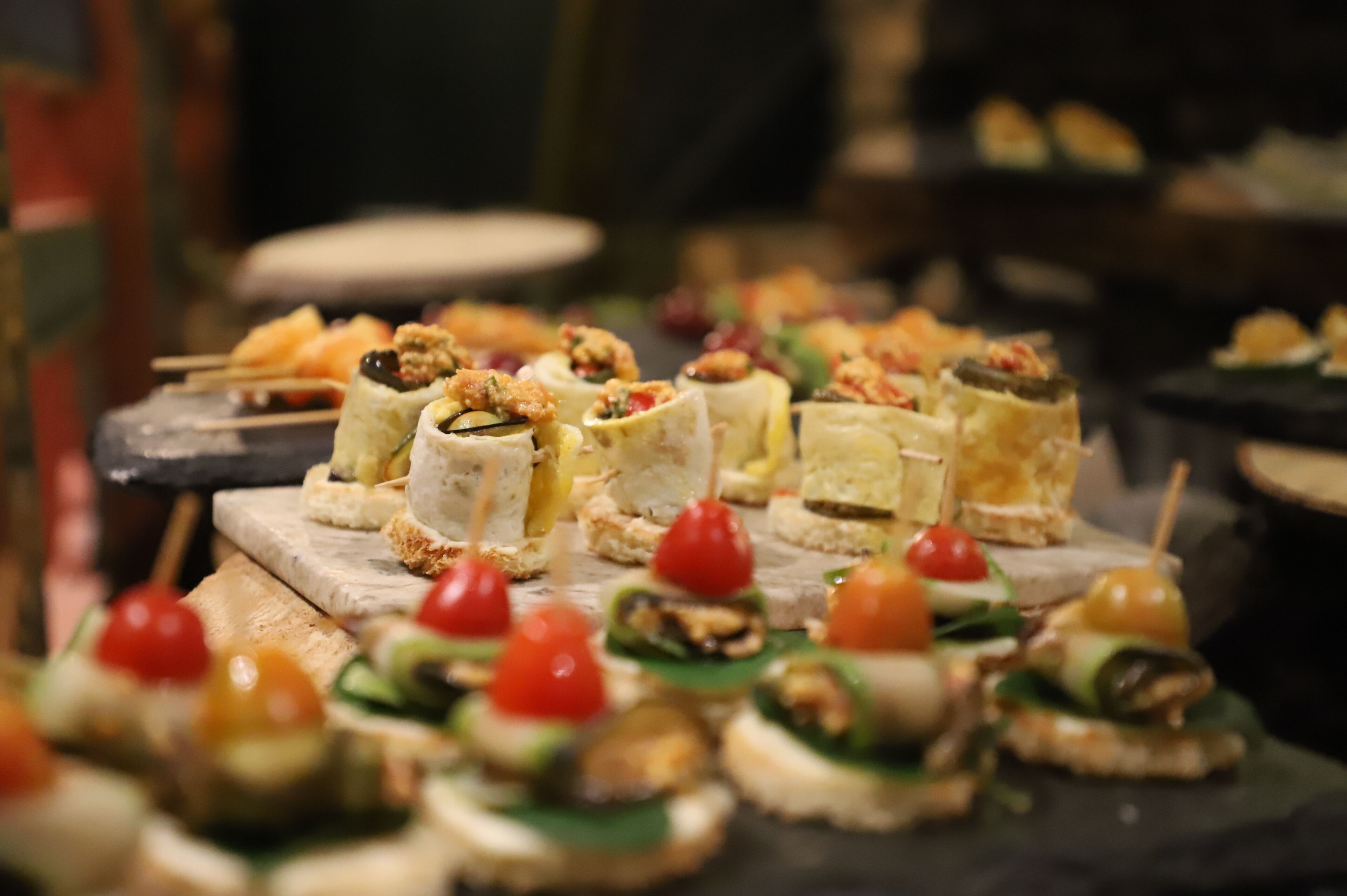Verschiedene Vorspeisen auf einem Holzbrett angerichtet, darunter Speisen mit Nüssen, Käse und Cocktailtomaten.