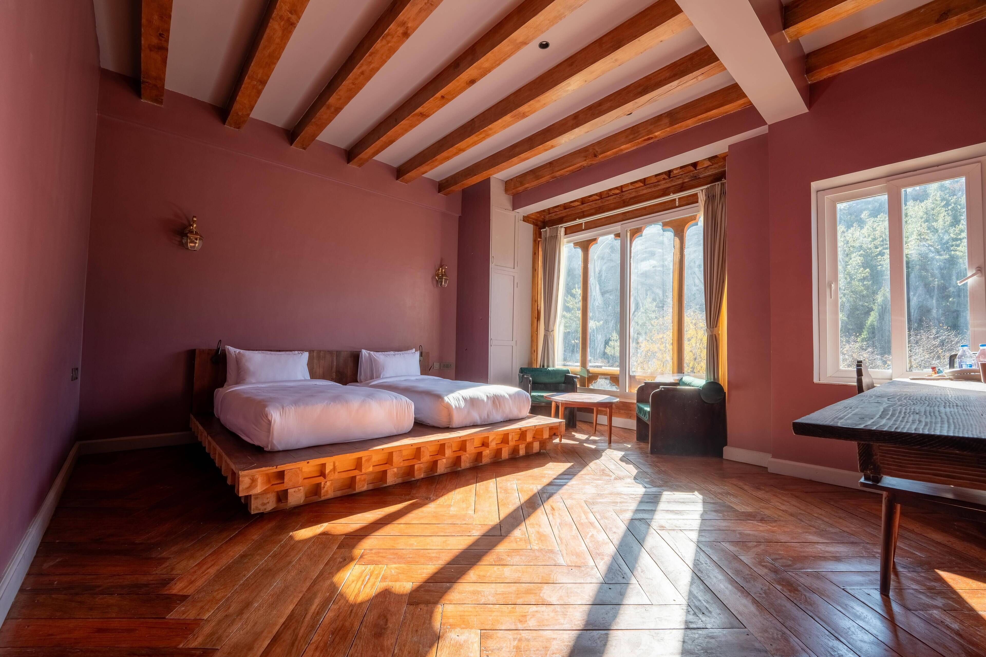 Quarto com estrutura de cama de madeira, uma mesinha e janela com vista para árvores.