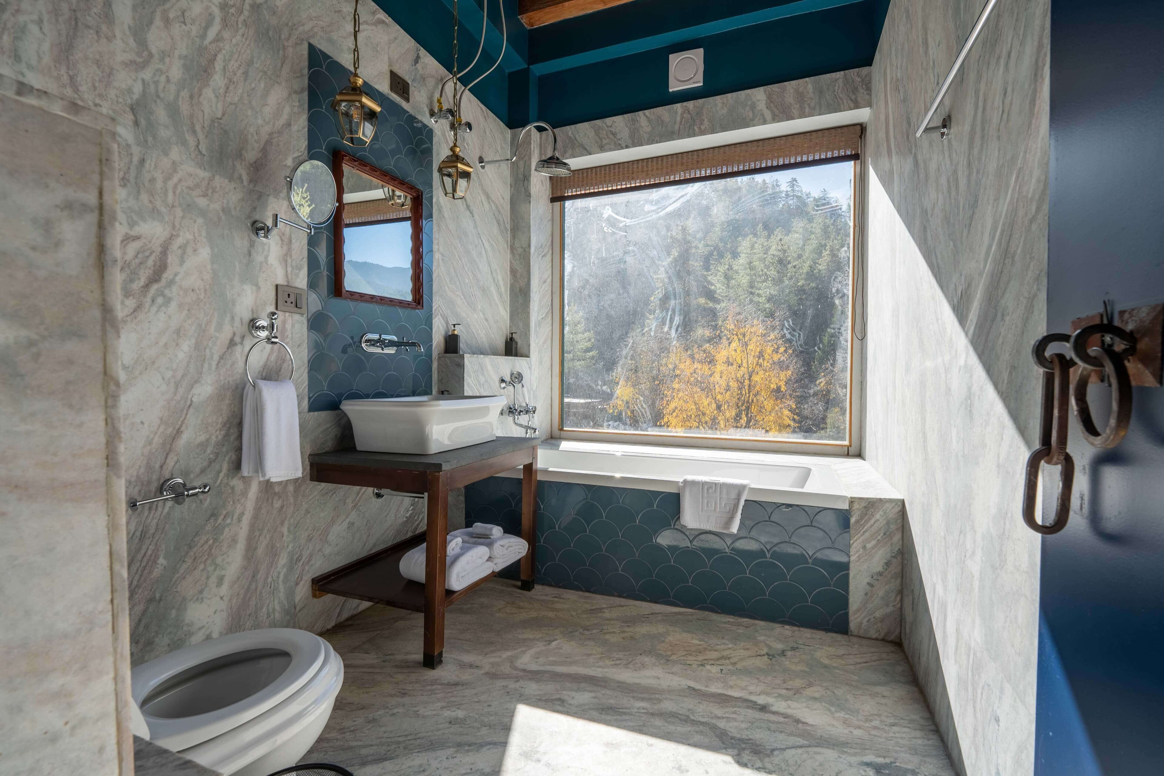 Une salle de bain avec des toilettes, un lavabo et une fenêtre donnant sur des arbres aux couleurs automnales.