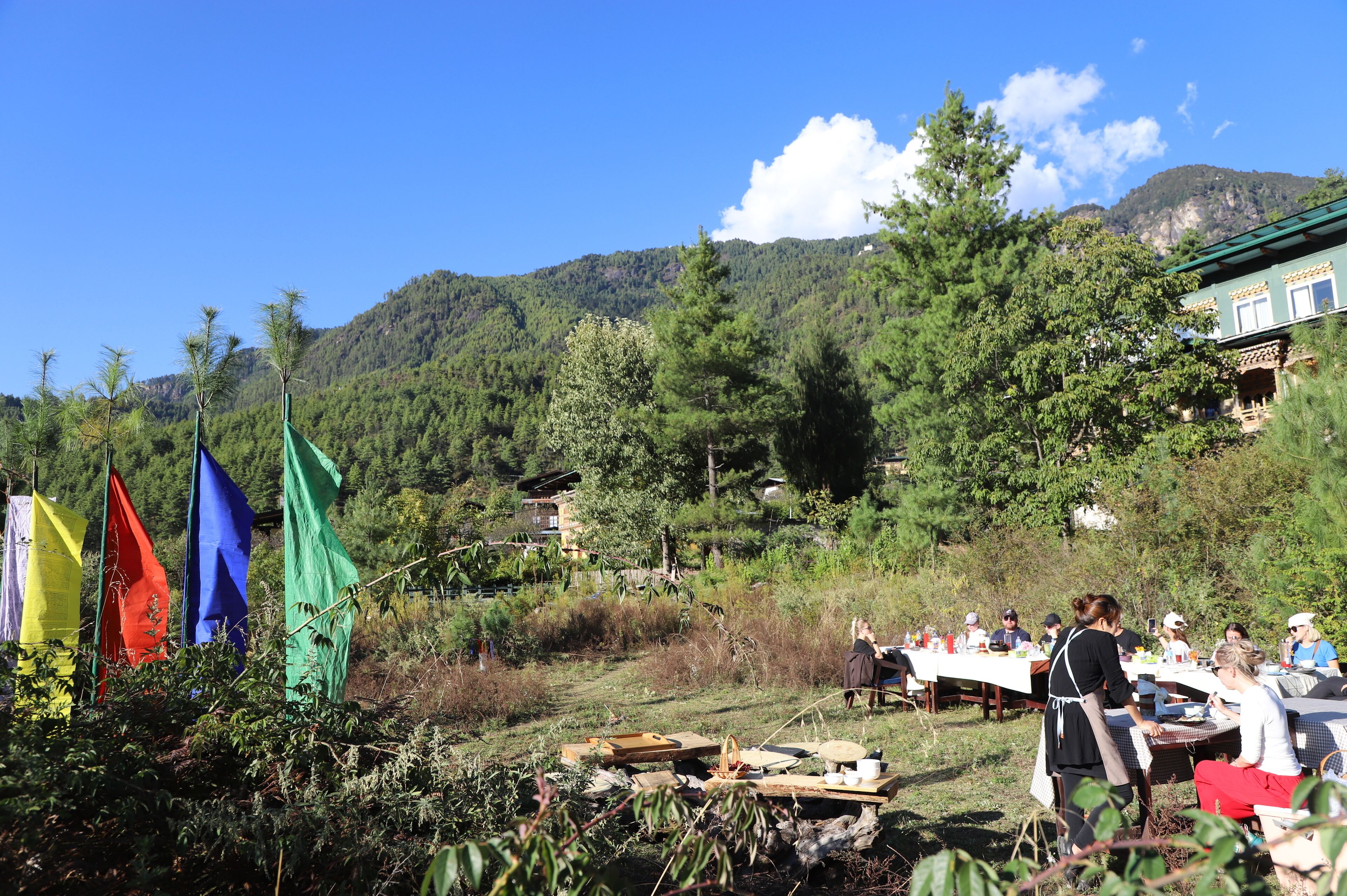 An outdoor dining area with tables set up in a natural setting, surrounded by trees and mountains.