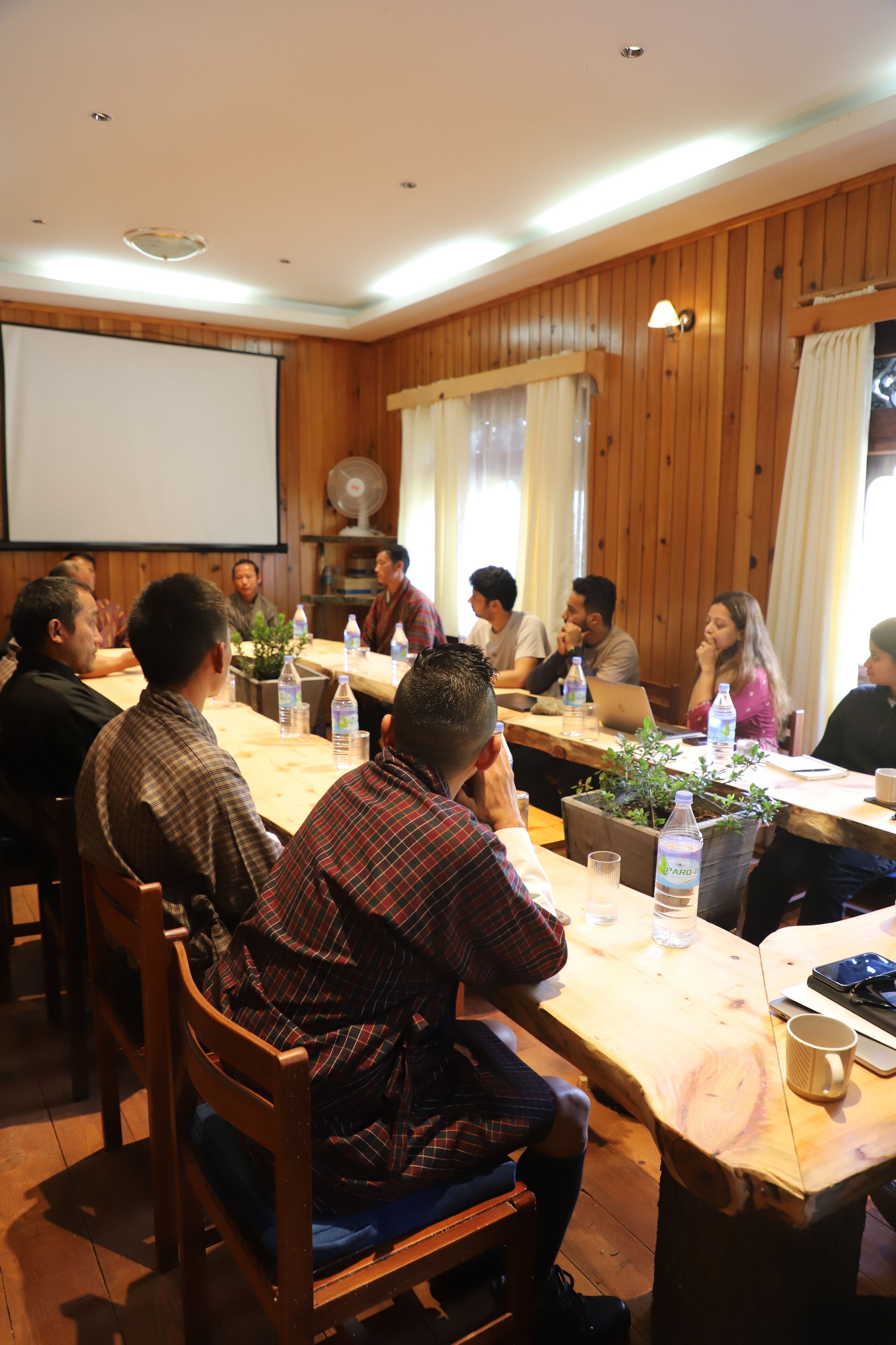 A conference room with wooden paneling, a projector screen, and tables with water bottles and laptops.