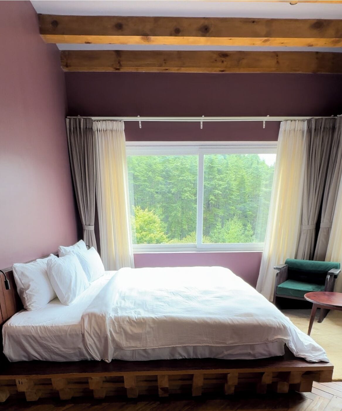 Un dormitorio con una ventana grande, una cama, una silla y una mesita.