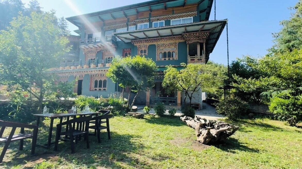 Un bâtiment traditionnel doté d’un balcon, entouré d’un jardin agrémenté de tables et de chaises.