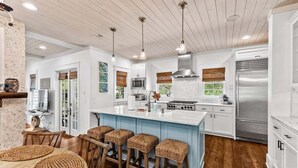 Una cocina moderna con una isla central, taburetes de madera y un refrigerador de acero inoxidable.