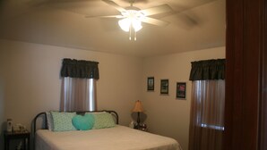 Un dormitorio con cama, mesita de noche, lámpara y ventilador de techo.
