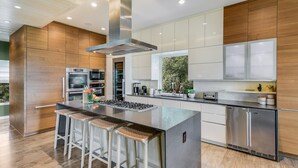 A modern kitchen with a central island, stainless steel appliances, and wooden cabinetry. - Above Capitol View I Skyline Views I Pool/Spa I Events I Weddings (Austin)