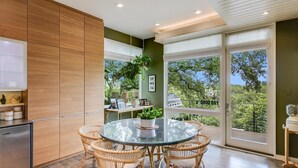 A modern kitchen with a round glass table and wicker chairs, a built-in refrigerator, and a view of a balcony with greenery. - Above Capitol View I Skyline Views I Pool/Spa I Events I Weddings (Austin)