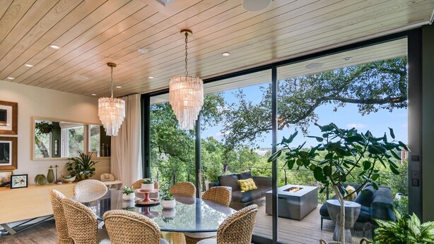 A modern dining area with wicker chairs, a glass table, and a view of the outdoors. - Above Capitol View I Skyline Views I Pool/Spa I Events I Weddings (Austin)