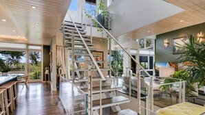 A modern interior with a wooden staircase, a dining area with bar stools, and a yellow ottoman. - Above Capitol View I Skyline Views I Pool/Spa I Events I Weddings (Austin)
