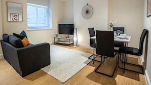 Un salon moderne avec un canapé noir, un téléviseur, une table à manger avec des chaises et une grande fenêtre.