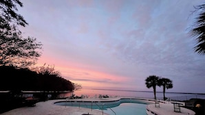 Uma área de piscina com espreguiçadeiras e vista para o mar ao pôr do sol.