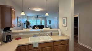 Uma cozinha moderna com ilha central, luminárias pendentes e vista para a sala de estar.