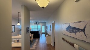 Um corredor com um candelabro, uma área de jantar com mesa e cadeiras, um espaço de cozinha com pia e armários, e um grande quadro de um tubarão na parede.