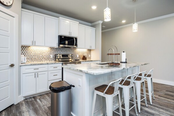 A modern kitchen with white cabinets, a stainless steel microwave, and a marble island with bar stools. - Pet-Friendly Waterfront Townhome | Plunge Pool & Boat Dock (Corpus Christi)