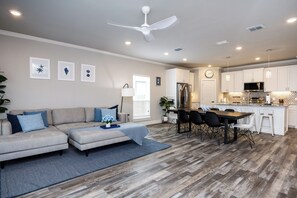 A modern living room with a sectional sofa, dining area, kitchen, and ceiling fan. - Pet-Friendly Waterfront Townhome | Plunge Pool & Boat Dock (Corpus Christi)