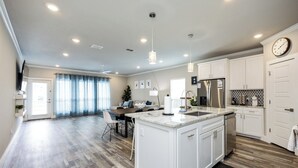 Une cuisine moderne avec des meubles blancs, un îlot central et un coin repas comprenant une table et des chaises.