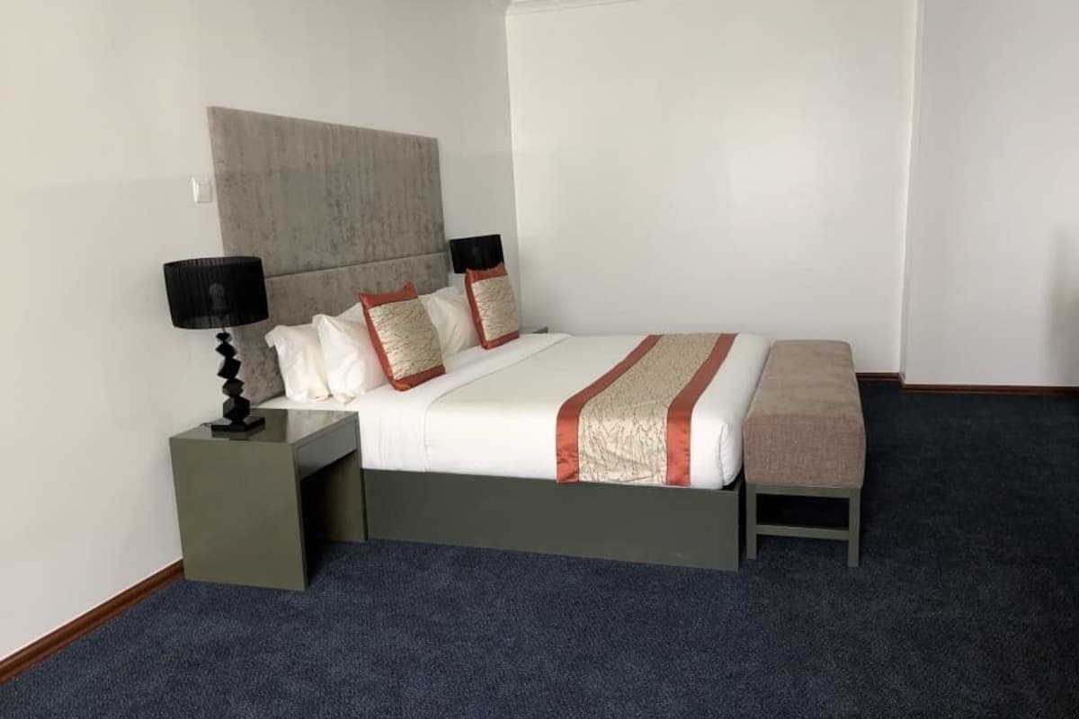 Una habitación de hotel con cama, mesitas de noche, lámpara y un banco.