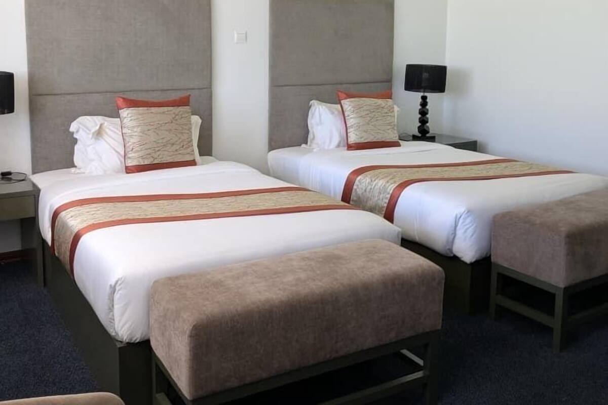Una habitación de hotel con dos camas, una mesita de noche, una lámpara y una silla.