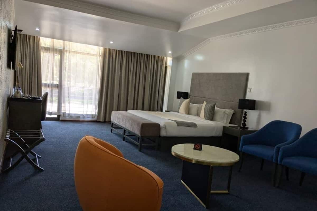 Una habitación de hotel con una cama, dos sillas, una mesita pequeña y un escritorio con una lámpara.