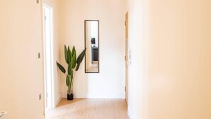 Een gang met een potplant, een spiegel en een deur naar een andere kamer.